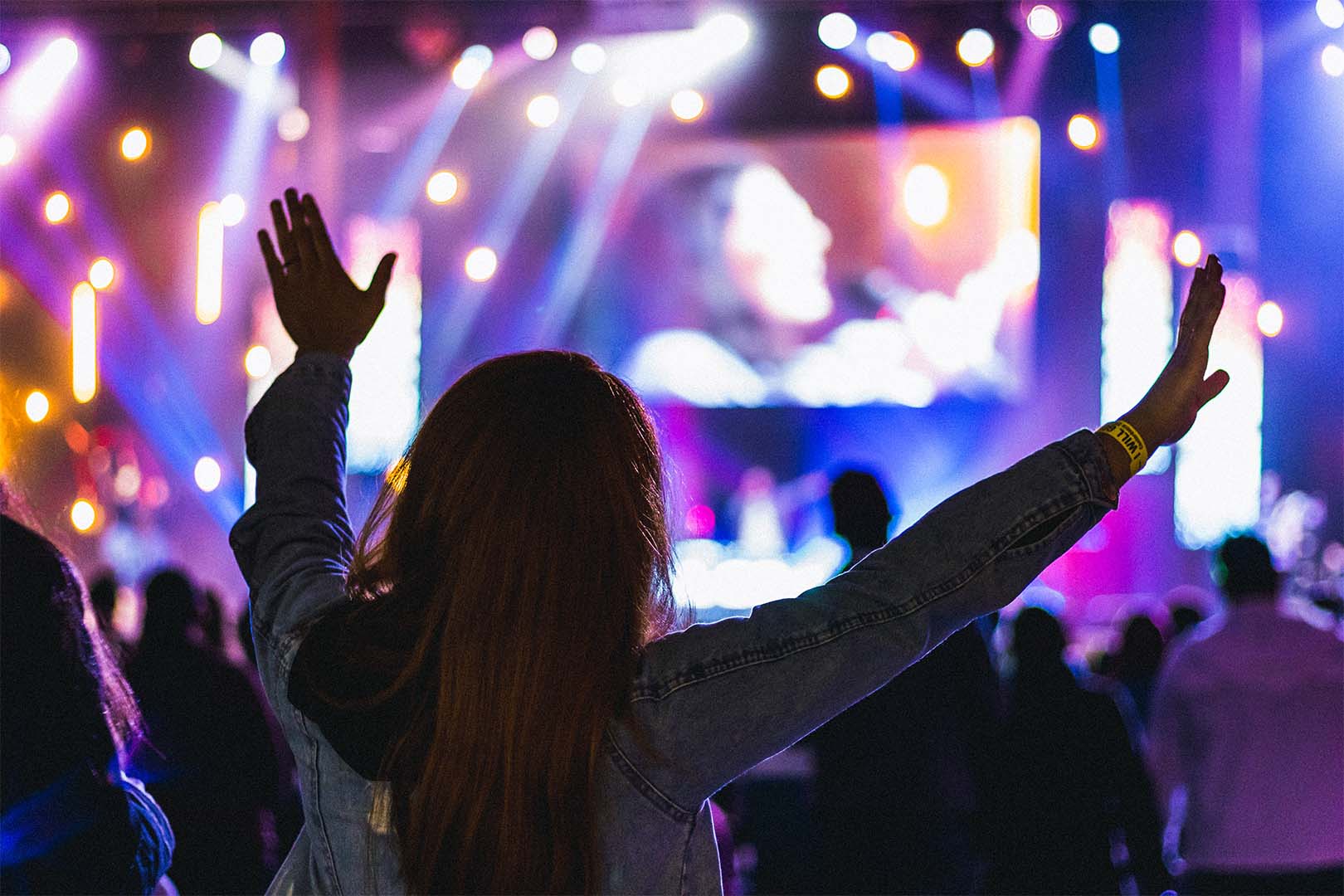 Woman raises hands at a worship event in a church.